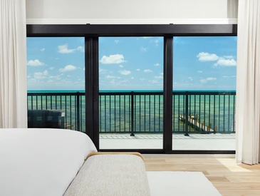 Marco de puerta corrediza de vidrio PGT SGD770 que enmarca la vista del balcón frente al mar desde un luminoso dormitorio costero