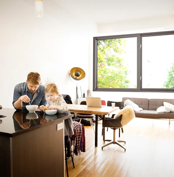 Un hombre y su hija disfrutan del desayuno en una habitación con ventanas resistentes a los impactos y que amortiguan el ruido