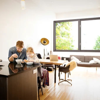Un hombre y su hija disfrutan del desayuno en una habitación con ventanas resistentes a los impactos y que amortiguan el ruido