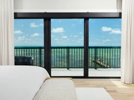 Marco de puerta corrediza de vidrio PGT SGD770 que enmarca la vista del balcón frente al mar desde un luminoso dormitorio costero